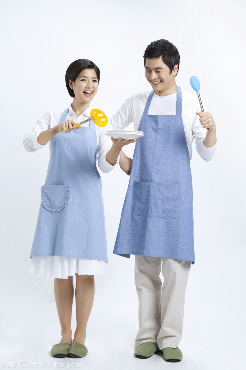 年輕夫婦在圍裙拿著廚房用具