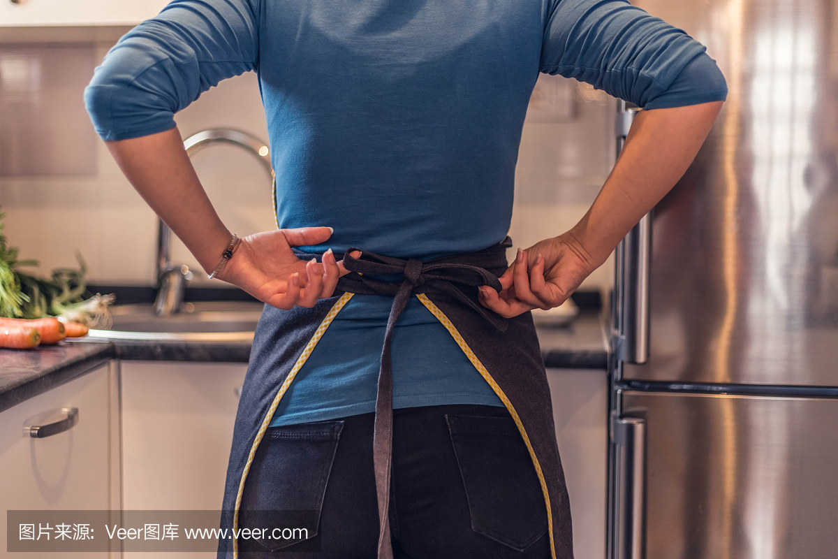緊縮的圍裙。廚房里穿著圍裙的漂亮女人。